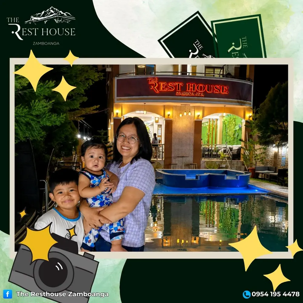 A mother holding her baby, with an older child beside her, in front of the lit resort and pool at night